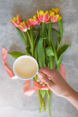 Coffee in hand, bouquet of tulips with a pink ribbon