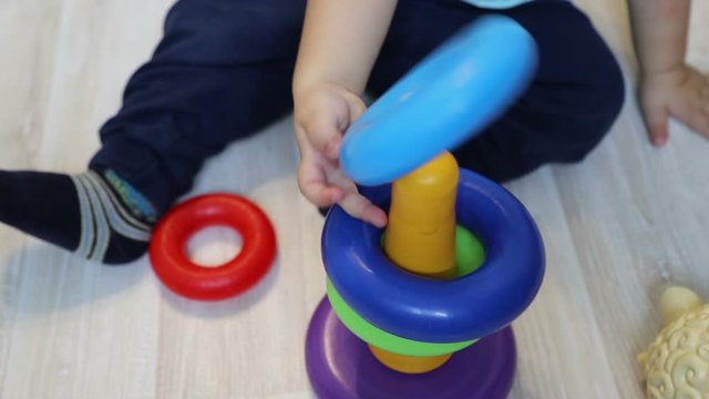 Little child (one year old) studies to collect colorful pyramid, close up.
