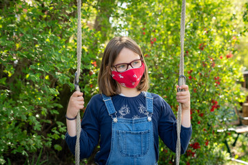 Child with face mask is sitting on a swing