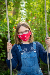 Child with face mask is sitting on a swing