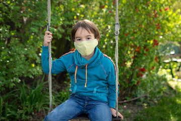 Child with face mask is sitting on a swing