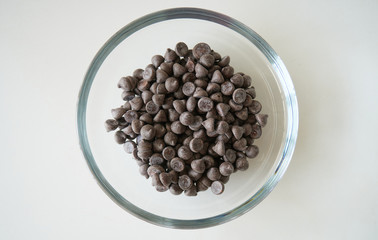 Dark chocolate chip drops in a glass bowl for baking 85% cocoa on a kitchen table, top view