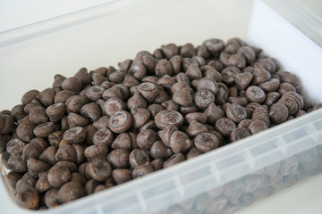 Chocolate chips 85 percent of cocoa dark chocolate drops in plastic box on a white kitchen table