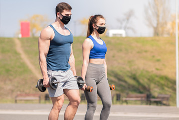 Athletic guy and a girl in medical masks lunges with dumbbells on a sports field during a pandemic. COVID-19. Health care.