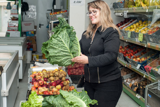 young blonde woman holding endive leaves in a grocery store.