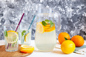 Lemonade in a glass jug on a white wooden table and glasses with straws.
