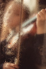 Girl with a violin behind a glass window with drops of water, low key. Music concept