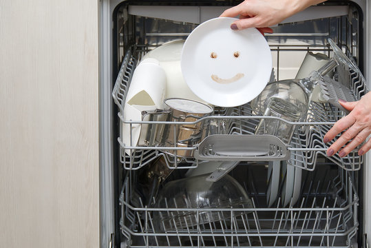 Fine washed dishes in the dishwasher. Integrated Dishwasher with white plates front vew and happy emotion on plate. Easy home cleaning concept