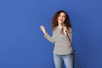 Young African-American woman singing on color background