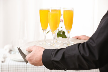 Waiter with glasses of tasty mimosa cocktail on tray at banquet