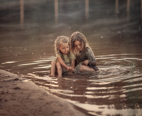 Two girls sisters sit in the water in the lake and play with each other