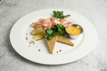 Plate with thinly sliced fat and mustard served with greens