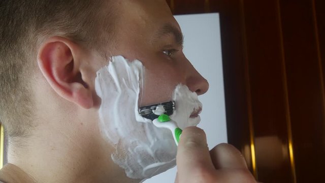 Man shaving with foam and manual razer. Close up of man shaving beard