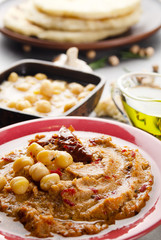 Fresh homemade Hummus in clay dish topped with olive oil, chickpeas, spices and sun dried tomatoes on stone table