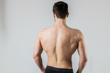 Back of a muscular bodybuilder athlete posing on a light background
