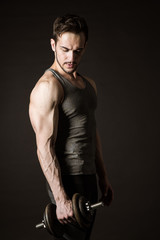 Fototapeta na wymiar Attractive male bodybuilder posing with dumbbells on a dark background