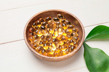Bowl of fish oil capsules on white wooden background