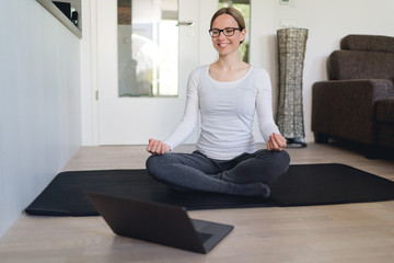 Frau meditiert zu Hause mittels online-Kurs und lächelt