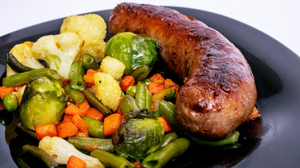 Grilled vegetables and sausage on a black plate