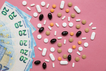 Close up of a 20 euro bills with several tablets with different color, shape e dimension as frame. Pink uniform paper background. Idea of addiction to drugs and money.