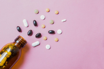 Close up of a dark glass bottle with several tablets with different color, shape e dimension. Pink uniform paper background.