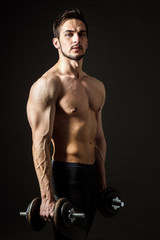 Fototapeta na wymiar Portrait of an attractive muscular athlete with dumbbells on a dark background