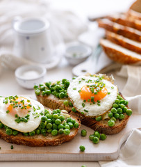 Vegetarian sandwiches made of sourdough bread with the addition of fried egg and stewed green peas on a white board, close up view