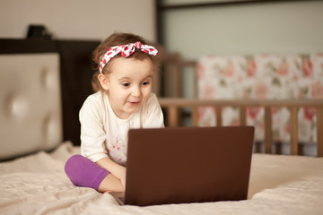 Little cute girl sitting on the bed and using a digital tablet laptop notebook. Online call friends or parents.