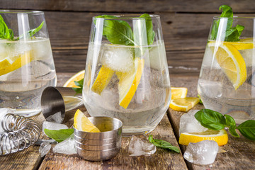 Boozy lemon basil lemonade, with fresh basil leaves, lemons and crushed ice, rustic wooden...