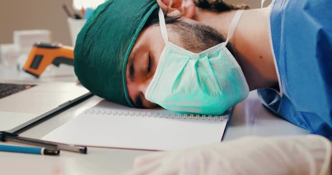 Medico o infermiere provato che dorme sulla scrivania o tavolo dell'ospedale dopo un turno in terapia intensiva a curare i malati di coronavirus.