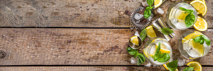 Boozy lemon basil lemonade, with fresh basil leaves, lemons and crushed ice, rustic wooden background copy space