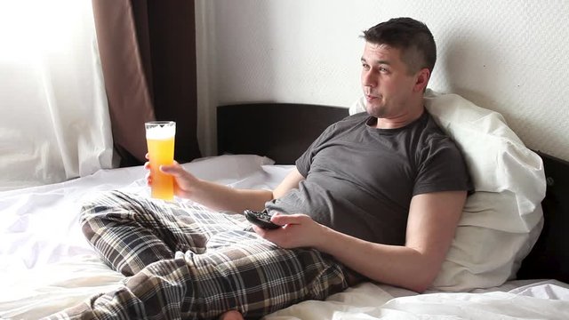a man in bed with a beer watching TV. Alcoholism from boredom during the Covid-19 coronavirus quarantine epidemic. Stay at home concept.