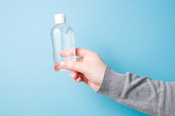 female hand holds a gel sanitizer in a transparent plastic small bottle with a white cap on a dark background copy space