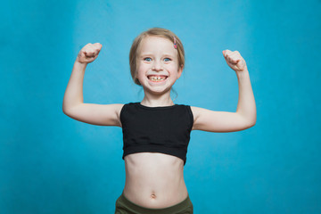 Happy pretten girl do sports and show muscles biceps on blue background.