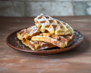 Homemade baking. Soft waffles lie slides on a small plate standing on a wooden brown background of a rutical kitchen