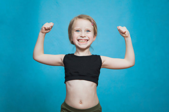 Happy pretten girl do sports and show muscles biceps on blue background.