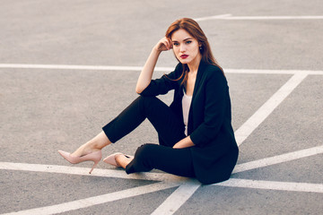Fototapeta premium Red-haired model in a suit sits in a parking lot in summer