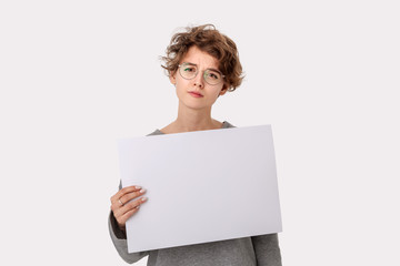 Fototapeta premium Concerned young woman with eyeglass holding empty blank paper board with copy space