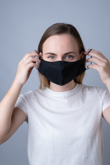 Woman puts a black medical mask on her face on a gray background