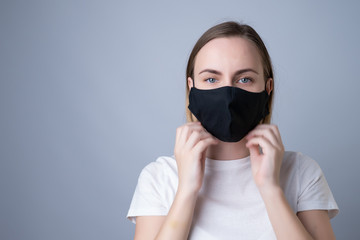 Woman puts a black medical mask on her face on a gray background