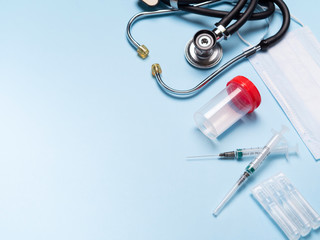 Stethoscope, disposable syringes, analysis tube, ampoules and protective sterile mask on blue background, medicine concept. Medical equipment layout with copy space. Coronavirus pandemia.
