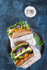 Healthy sandwiches with arugula, carrot, cheese, red cabbage, wrapped in craft organic paper on a dark blue background, space for text. Top view. Big Club sandwich concept, in rustic style.