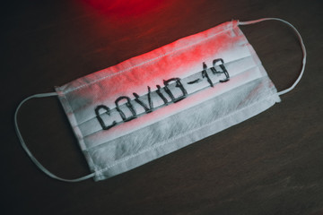 medical mask with the inscription "COVID-19" on a dark background with red light