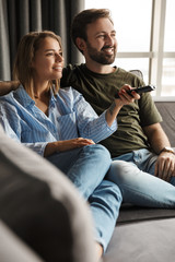 Obraz premium Photo of joyful couple watching TV and using remote control