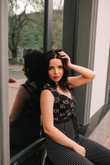 Obraz na płótnie Canvas Beautiful brunette in black overalls, suit, posing on a city street, against the background of a new modern building in dark colors