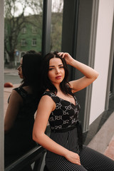 
Beautiful brunette in black overalls, suit, posing on a city street, against the background of a new modern building in dark colors