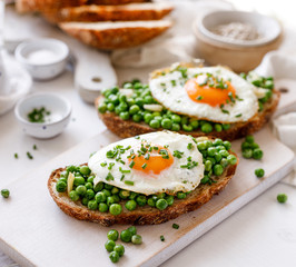 Fototapeta na wymiar Vegetarian sandwiches made of sourdough bread with the addition of fried egg and stewed green peas on a white board