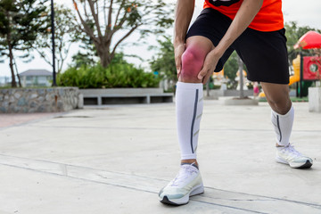 Close up on knee Injury. The man use hands hold on his knee while running in the park. space for text or design. highlight on injured area