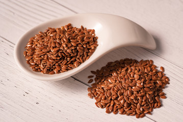 Flax seed close-up in a white glass dish and next to it is piled on the table .