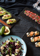 Four plates with appetizers, tartlets, canapes, bruschettas, tataki, on a black wooden background, a buffet table, copy space flat lay